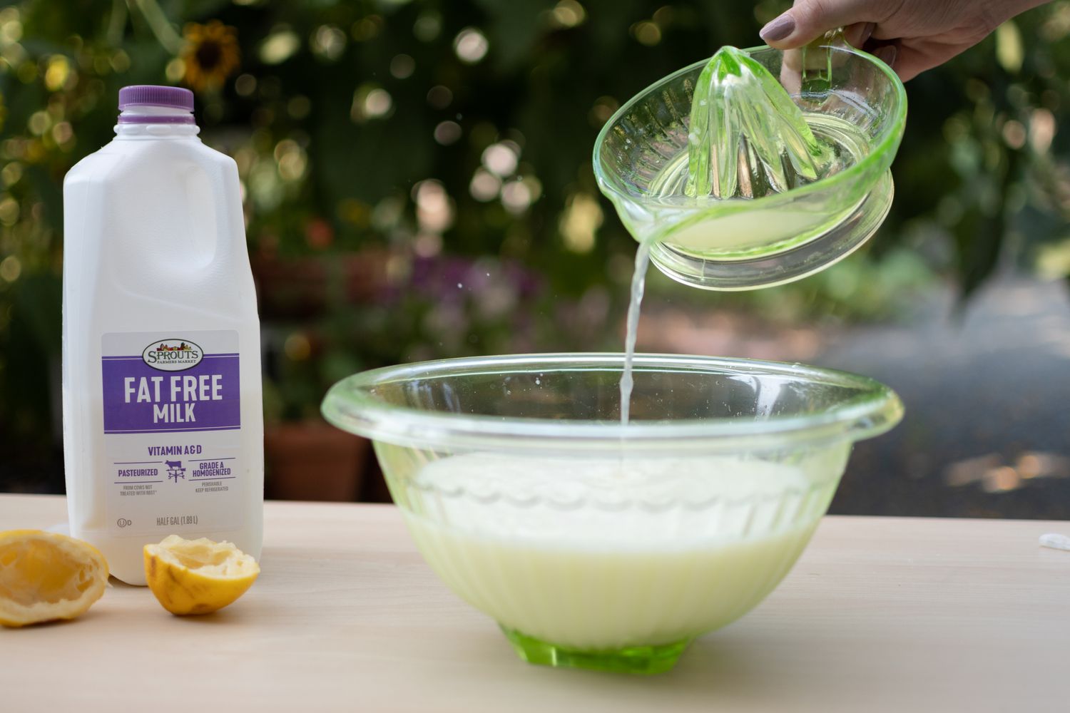Ausgepresster Zitronensaft in eine Glasschüssel mit Milch neben einem Milchkarton und Zitronenschalen gegossen