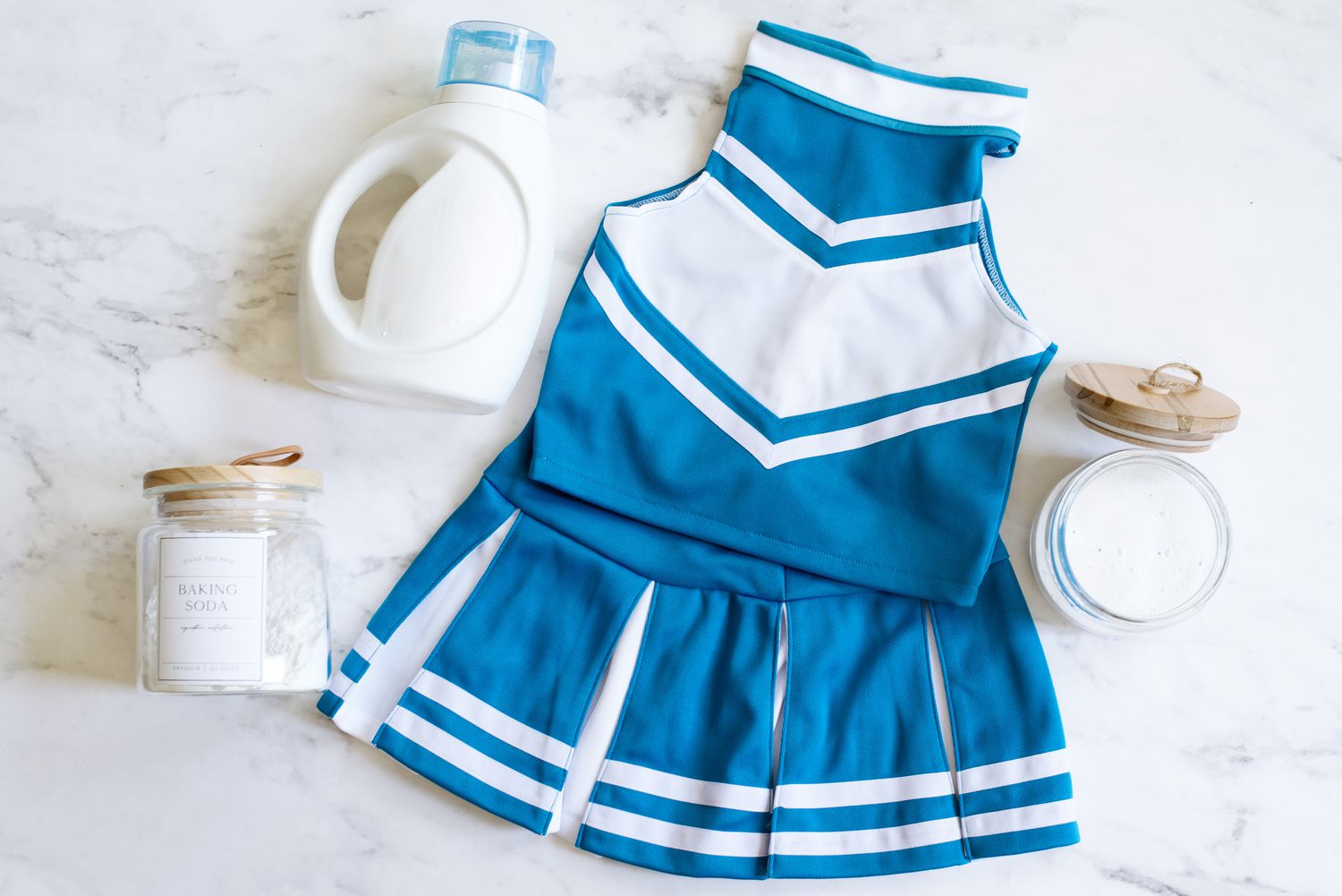 Uniforme de animadora azul y blanco junto a botella de detergente para la ropa y envases de vidrio de bicarbonato