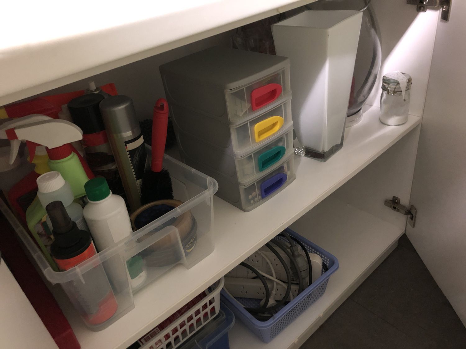 Un armario bajo el fregadero con artículos de limpieza y cestas.