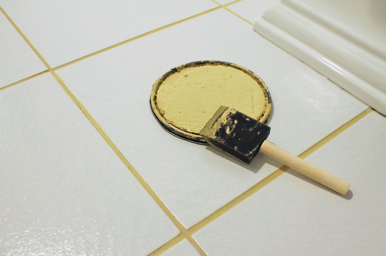 Piso de banheiro branco com um prato de rejunte de tinta amarela e pincel de espuma