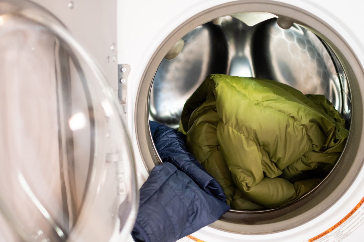 Grüne und blaue Daunenmäntel in der Waschmaschine vor der Tür