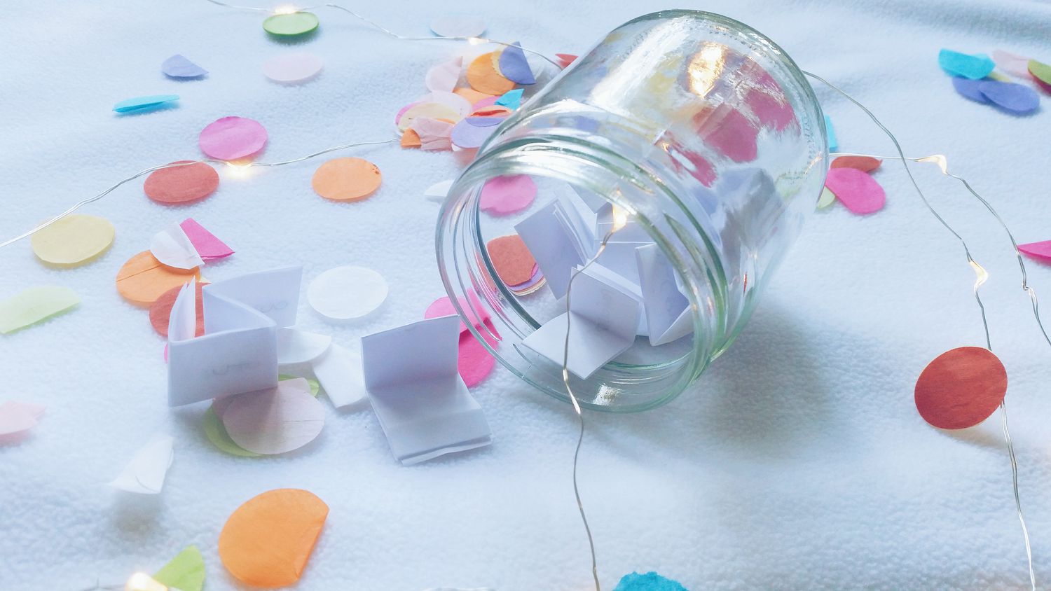 Wunschglas gefüllt mit Papierwünschen auf einem Tisch mit Konfetti