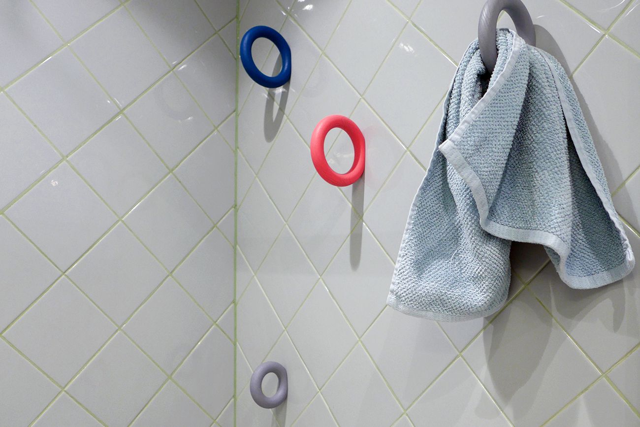 Chuveiro do banheiro com azulejos brancos e rejunte verde, e porta-toalhas multicoloridos