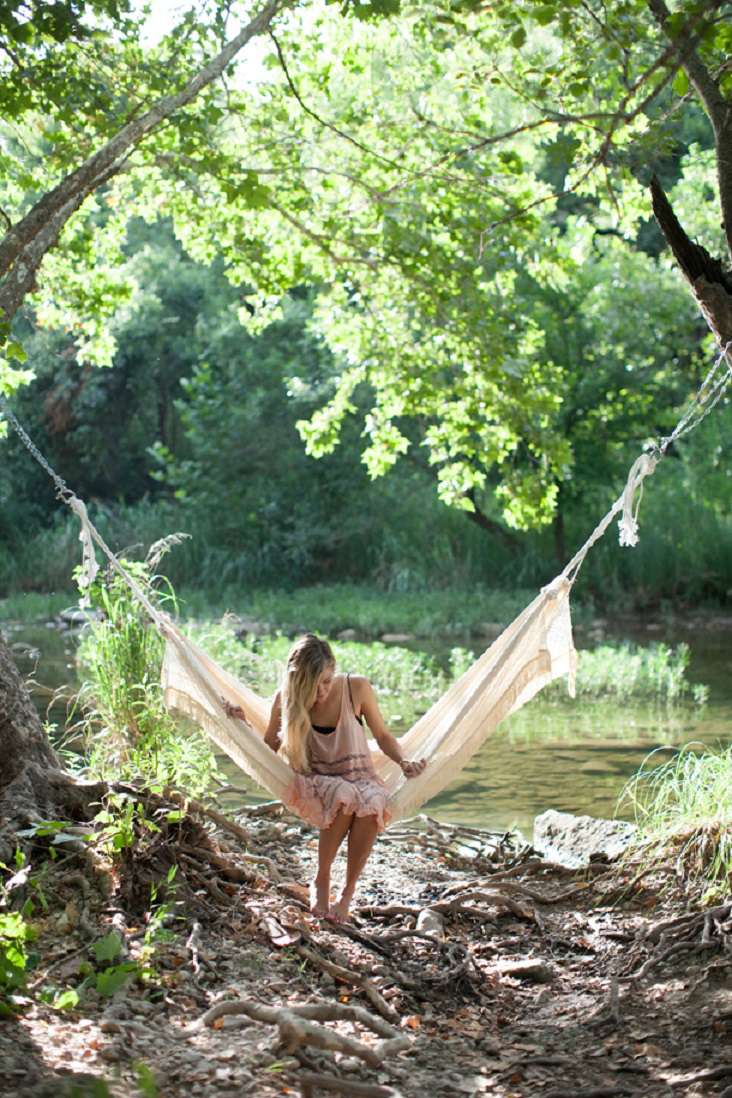 Uma garota sentada em uma rede de macramê perto de um riacho.
