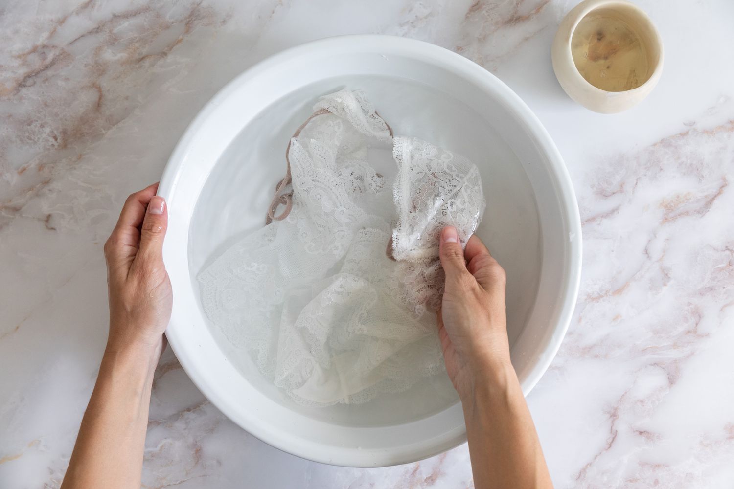 Weiße Spitzenkleidung, handgewaschen in einer weißen Schüssel mit Wasser und Feinwaschmittel