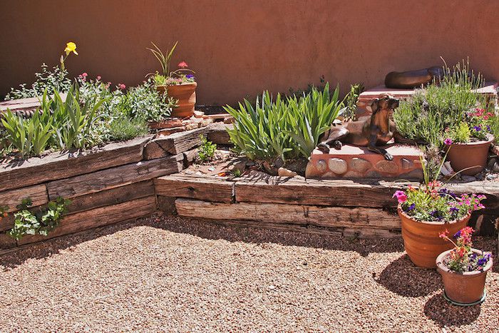 Jardim com vigas de madeira ao redor de canteiros elevados e plantas xeriscas, além de escultura de cachorro