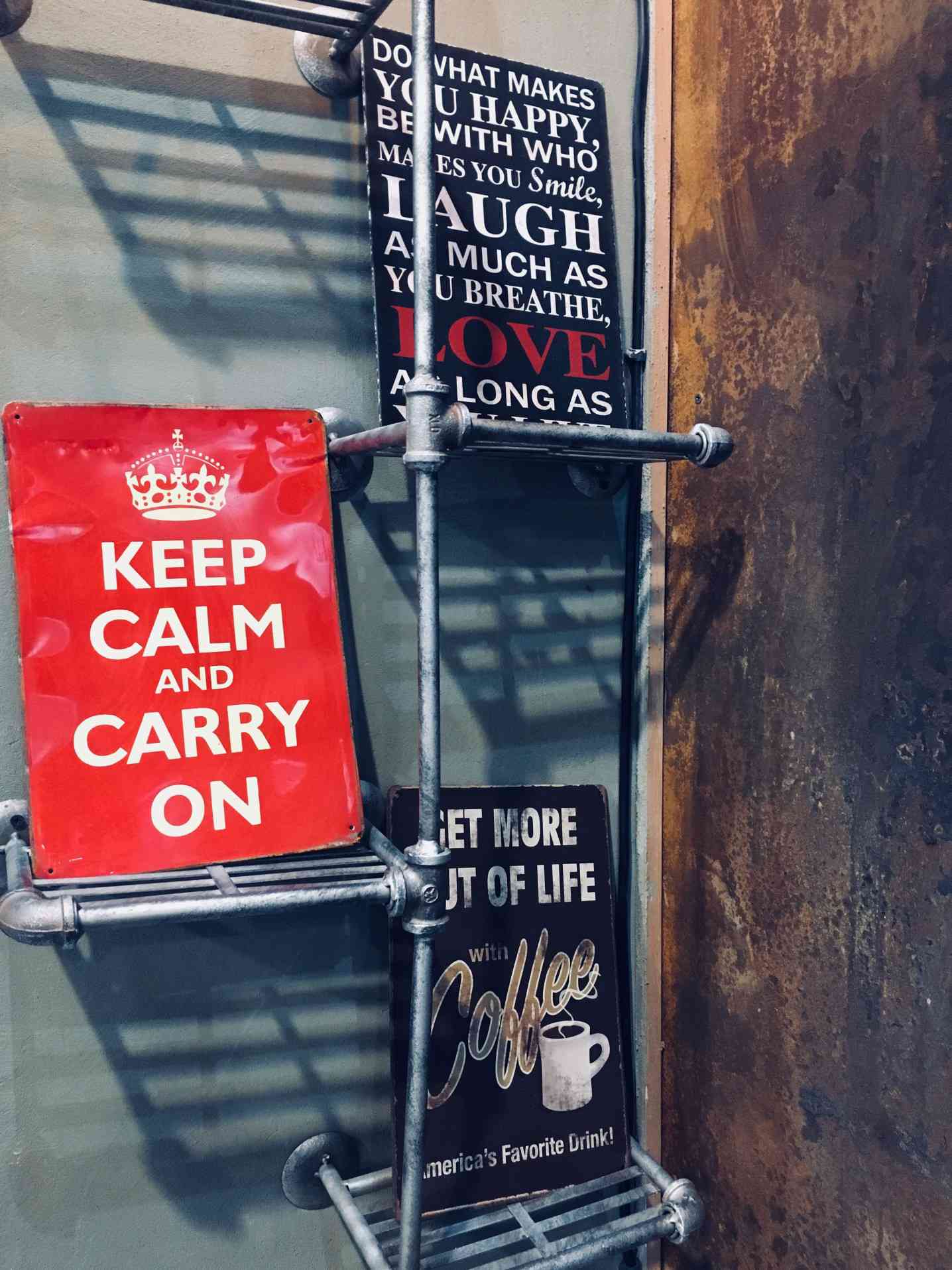 Placa vermelha Keep Calm and Carry On em uma prateleira com outras placas.