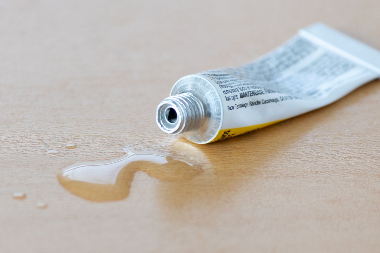 Super glue squeeze bottle open with super glue on wooden surface closeup