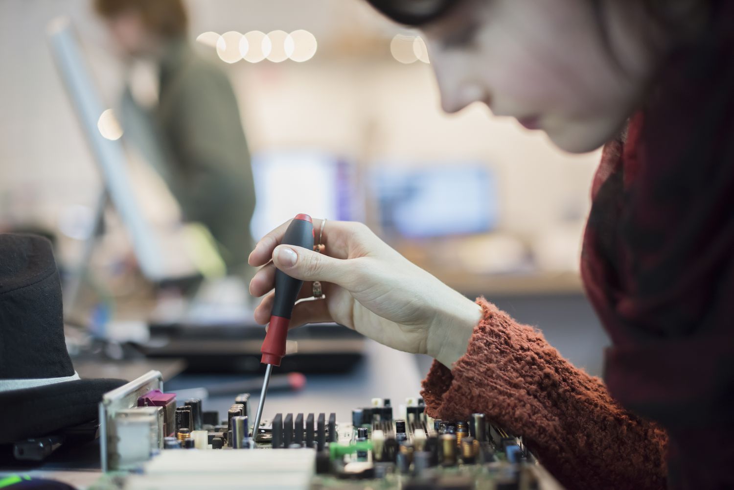 Computerwerkstatt. Eine Frau arbeitet mit einem elektronischen Schraubenzieher an einer Computerplatine.