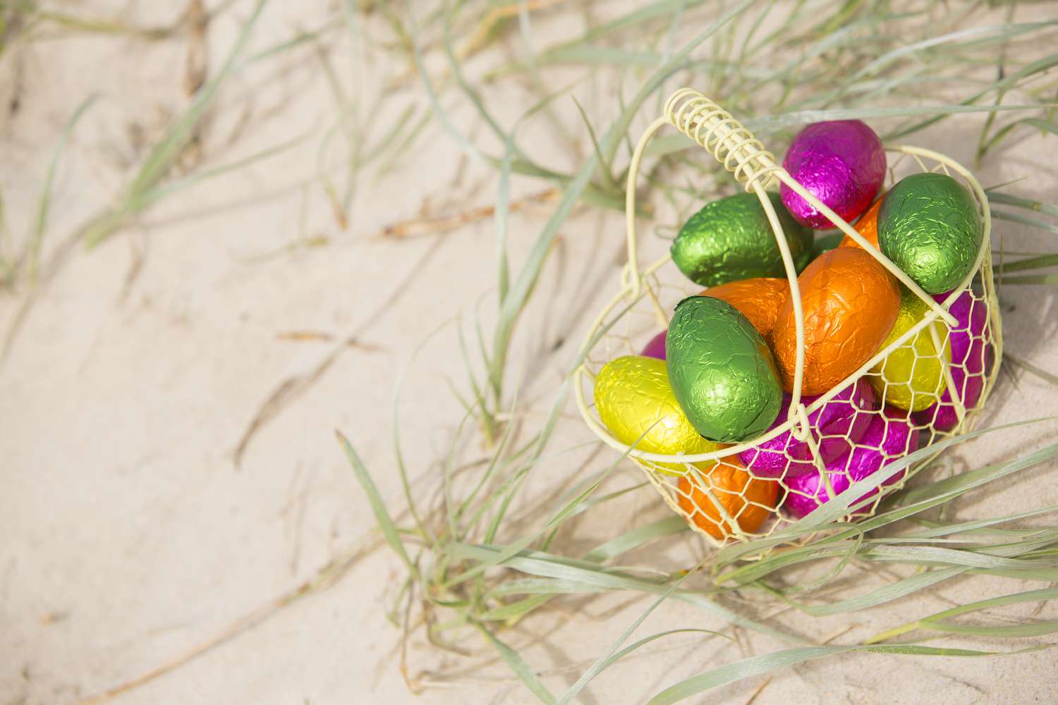 Kleines Körbchen im Strandsand mit bunten Ostereiern