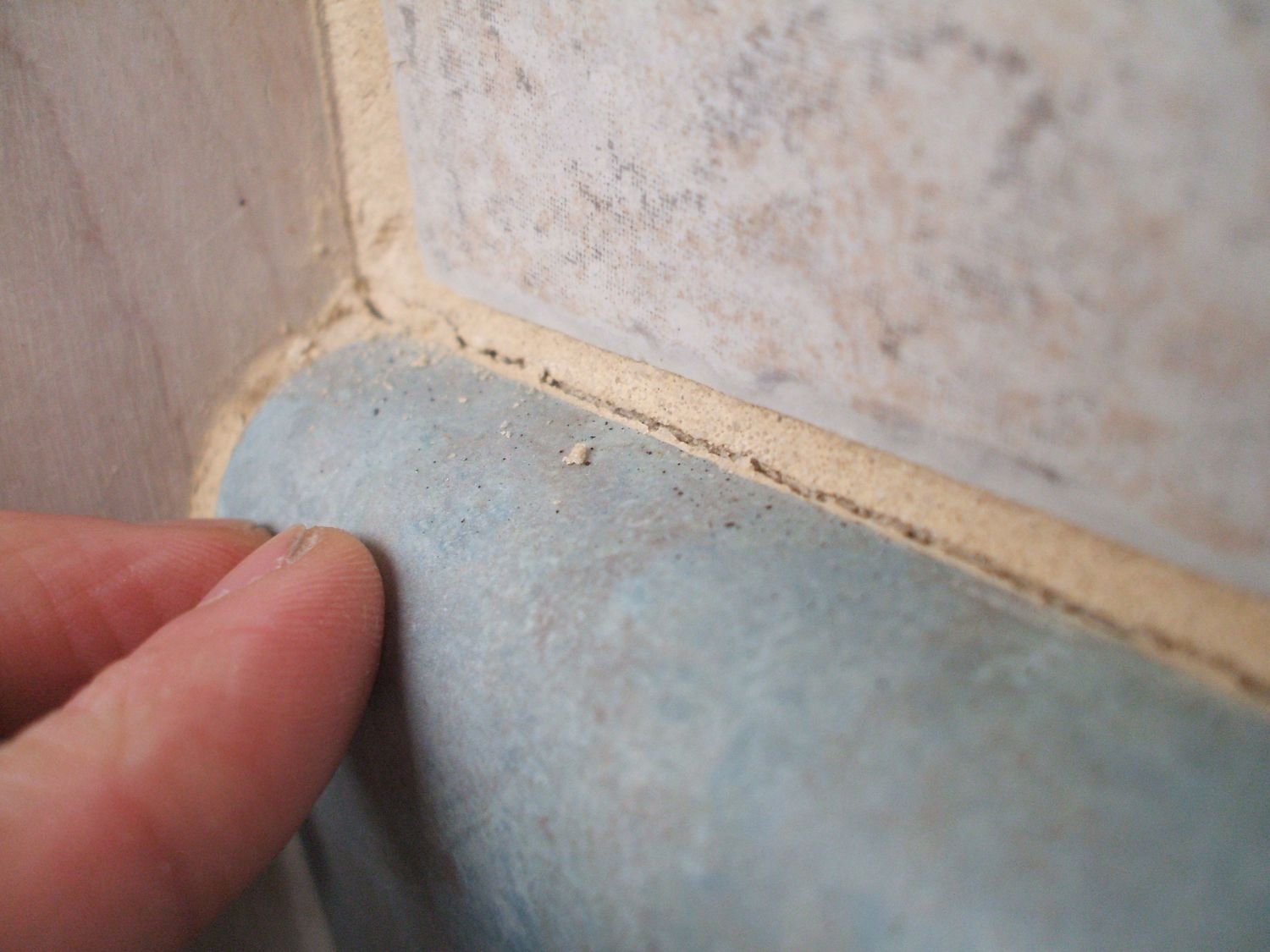 Hands putting grout between tile and non-tile materials