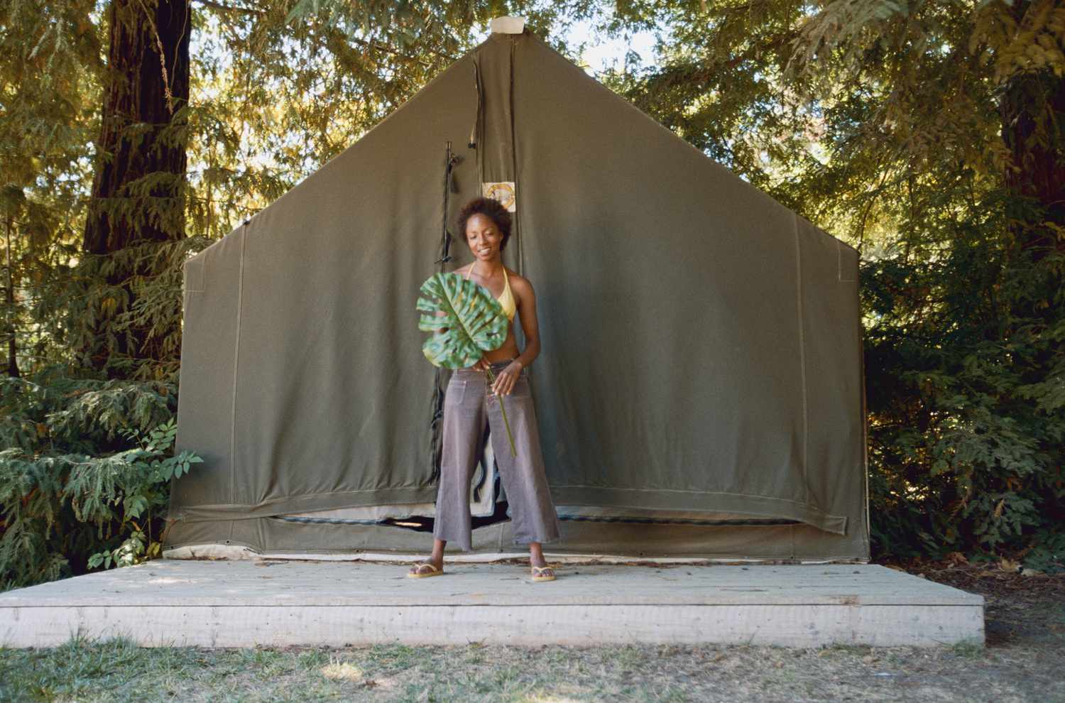 Woman holding leaf outside tent on concrete slab.