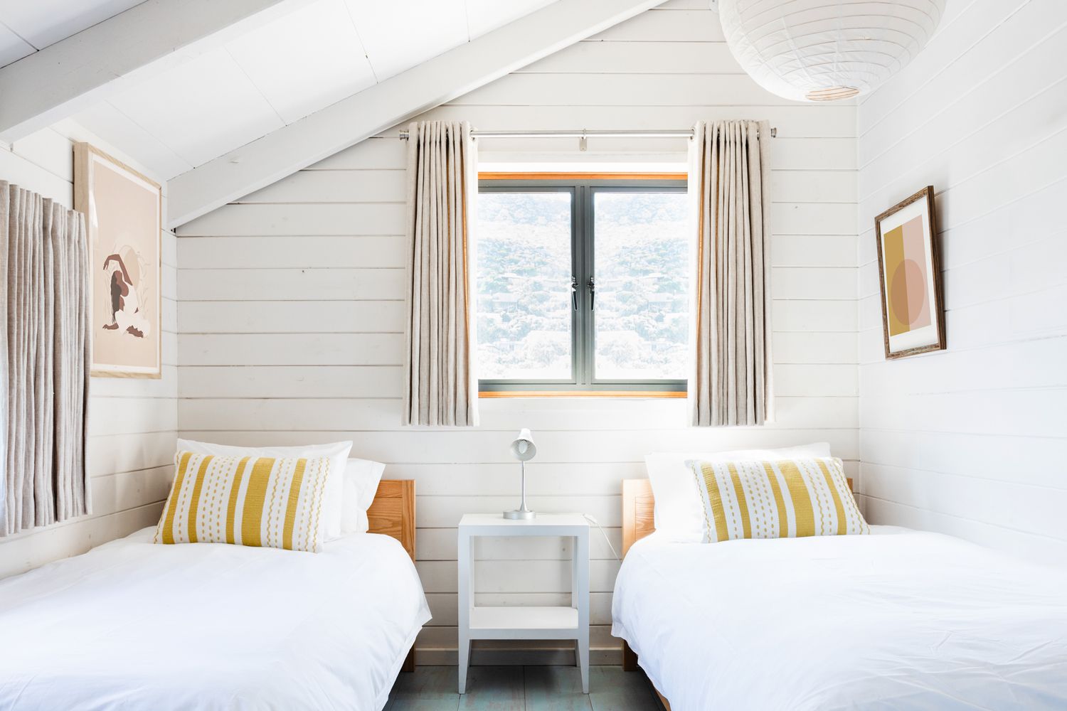 Dormitorio decorado con paredes de shiplap blanco y dos camas individuales bajo la ventana