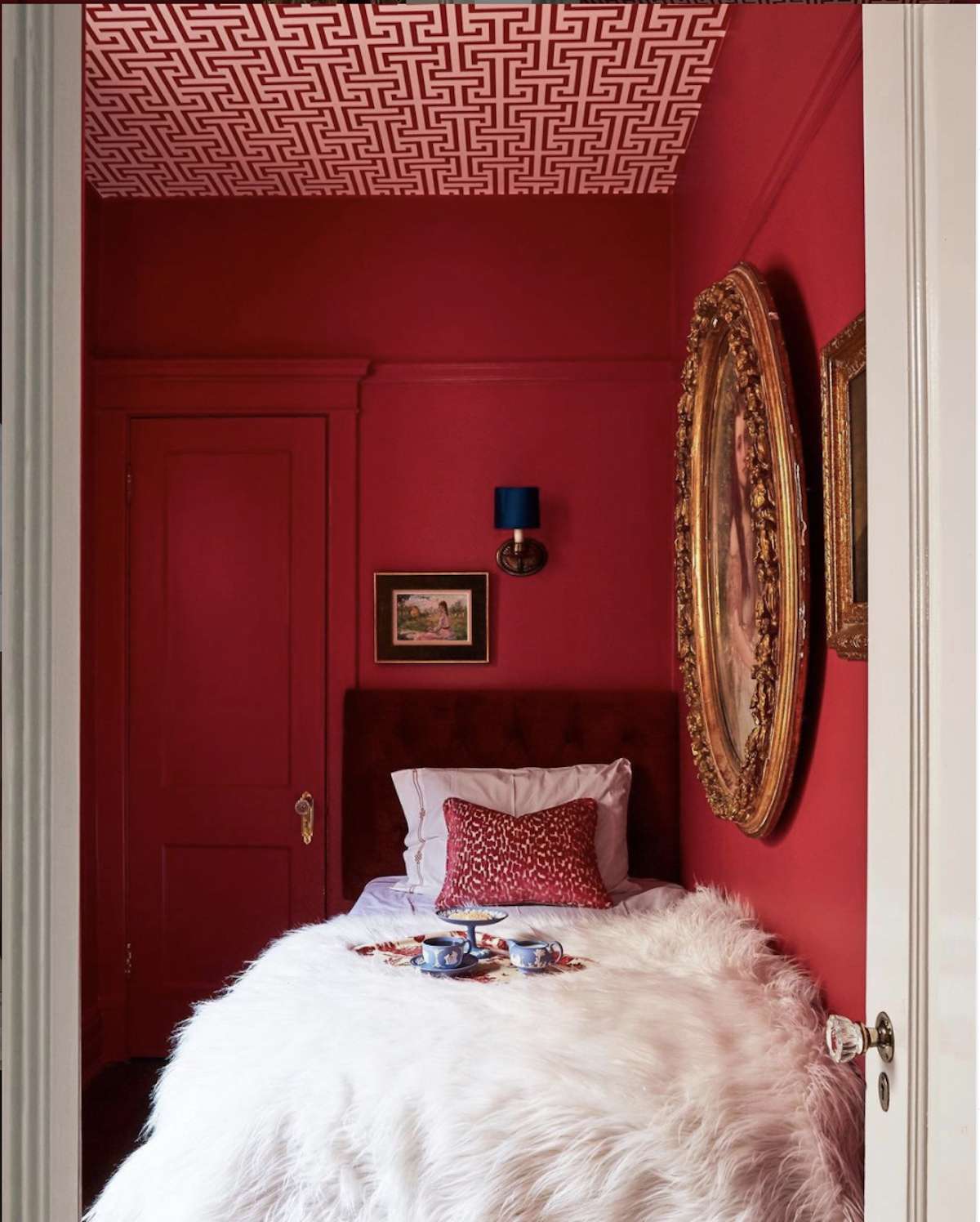 bedroom with red walls, red and white pattern ceiling, white fluffy blanket