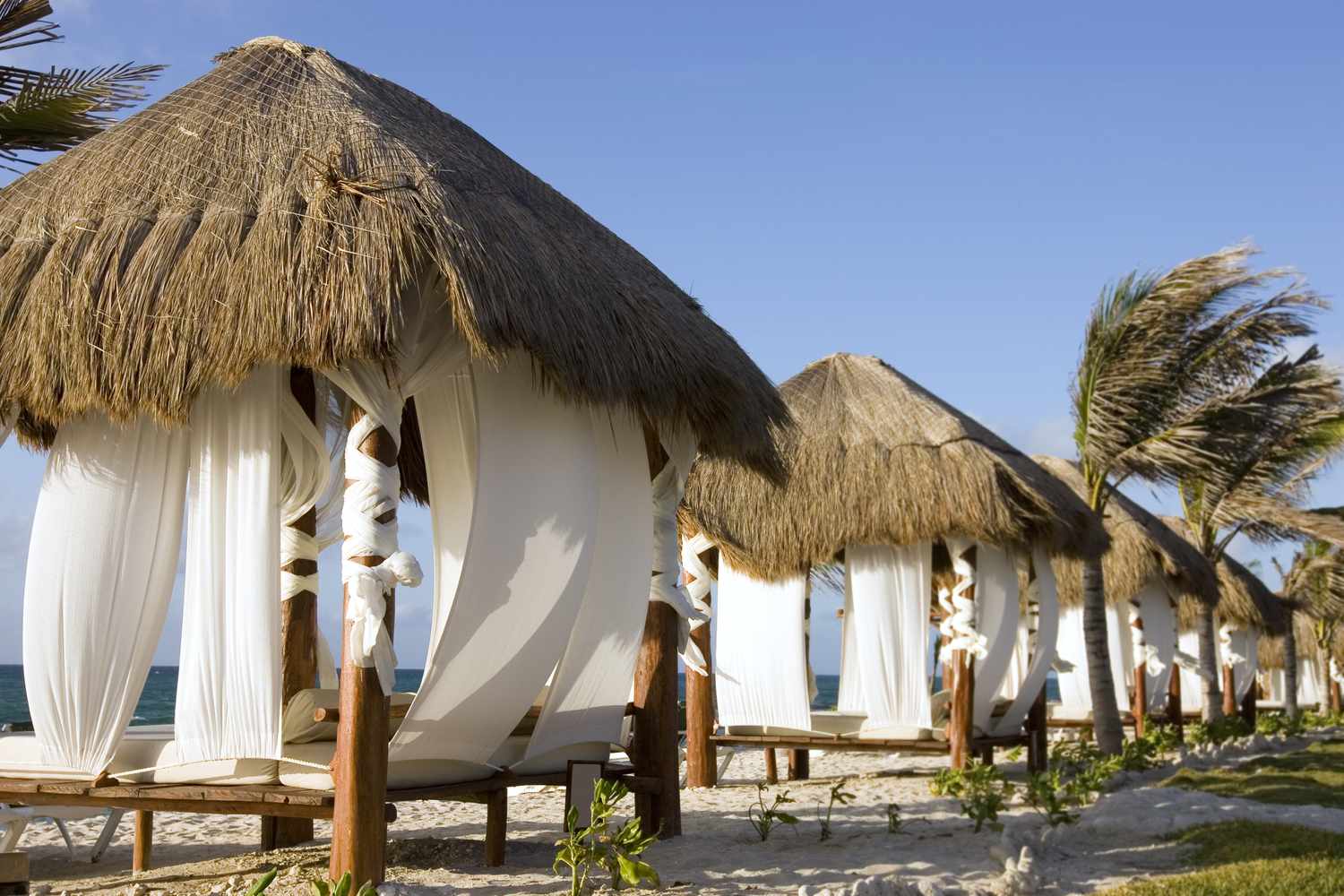 Strohgedeckte Cabanas mit Stoffwänden am Strand.