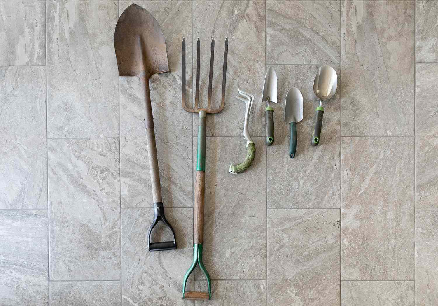 Werkzeuge zum Anlegen eines Gemüsegartens auf grauem Kachelboden