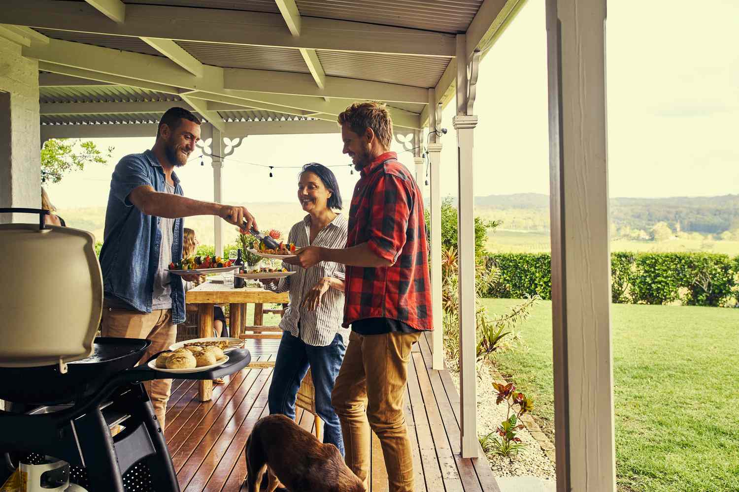 Mann serviert seinen Freunden das Mittagessen unter dem Dach einer Terrasse