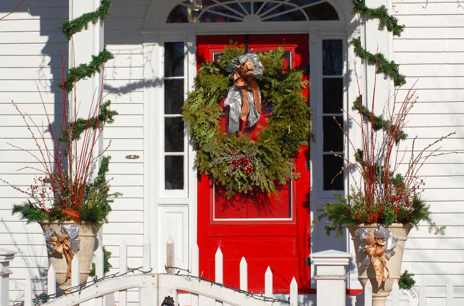 Columnas con guirnaldas y urnas con adornos navideños flanqueando una puerta principal con una corona.