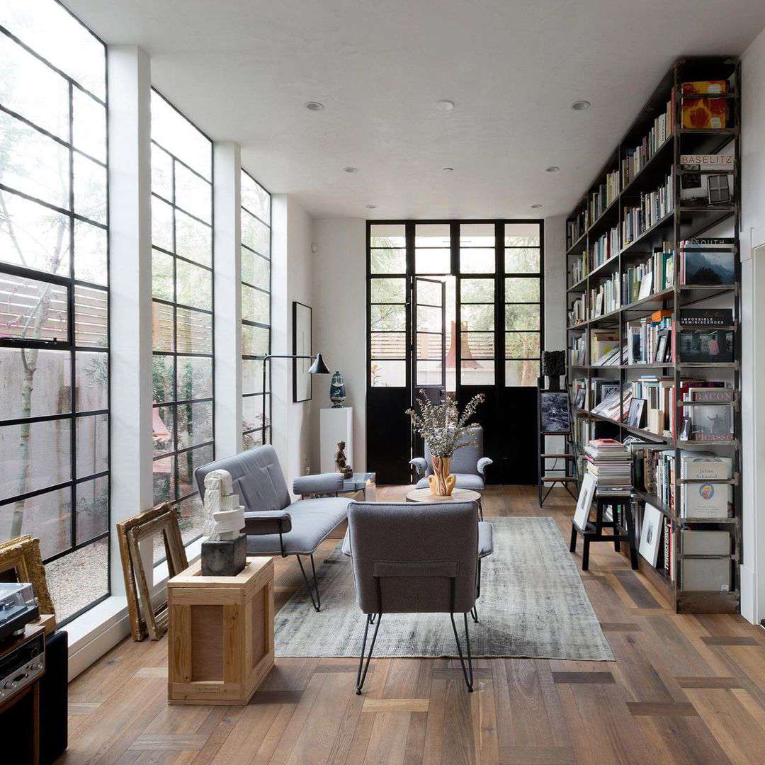 Un salon de style urbain avec de grandes fenêtres et un mur d'étagères remplies de livres.