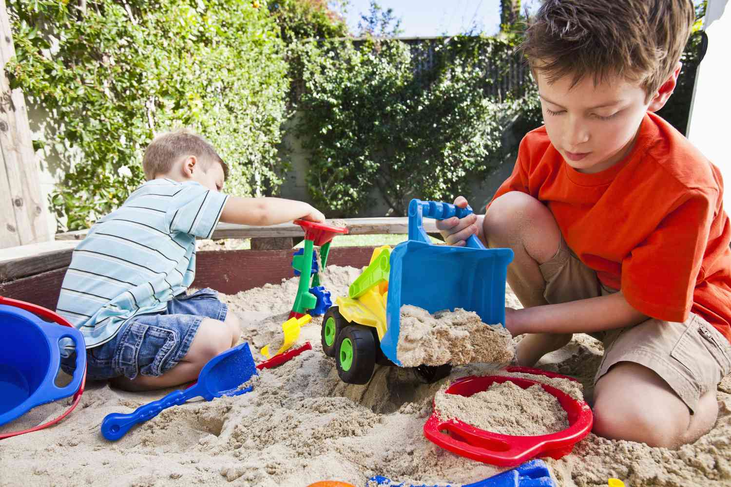 Dos niños jugando con camiones en un arenero.