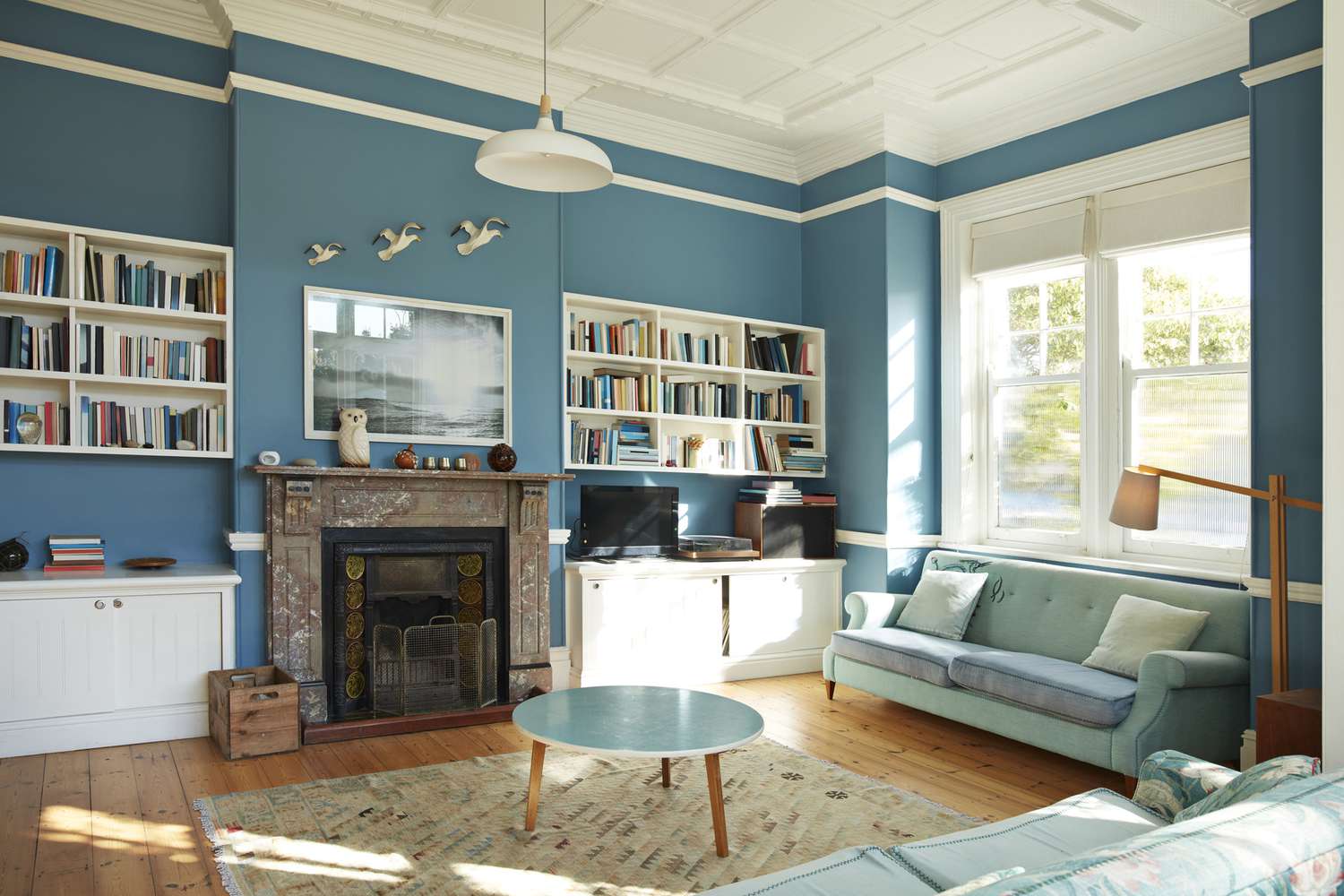 Sala de estar decorada com paredes azul-petróleo e estantes de livros