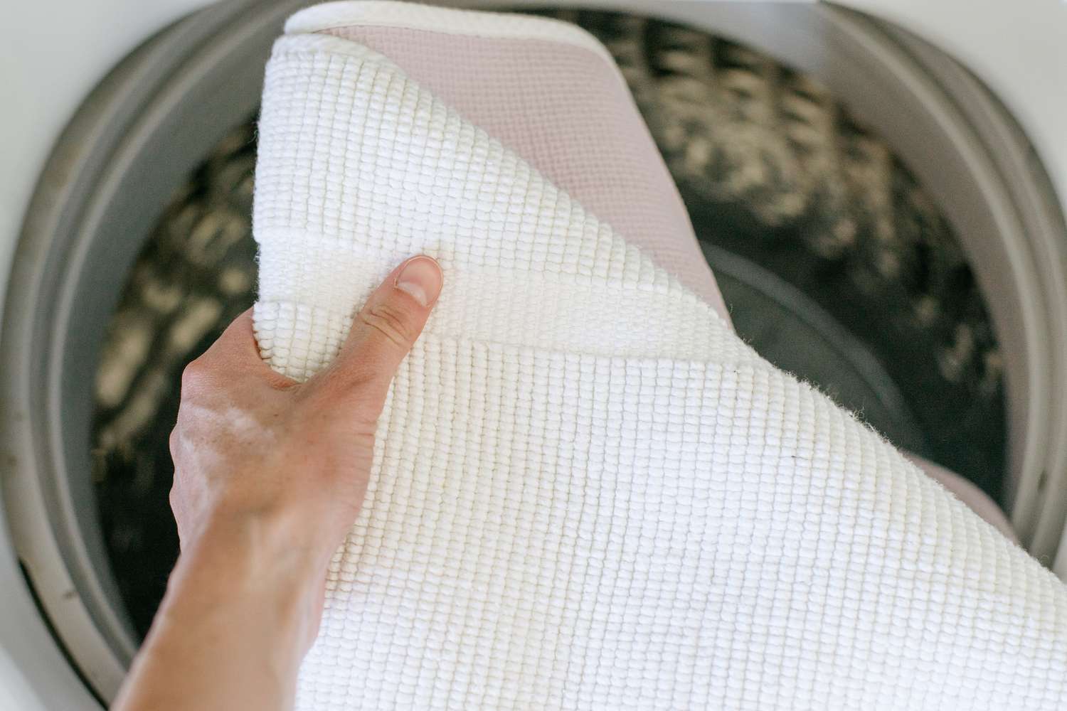 Weißer Teppich wird über die Waschmaschine gehalten