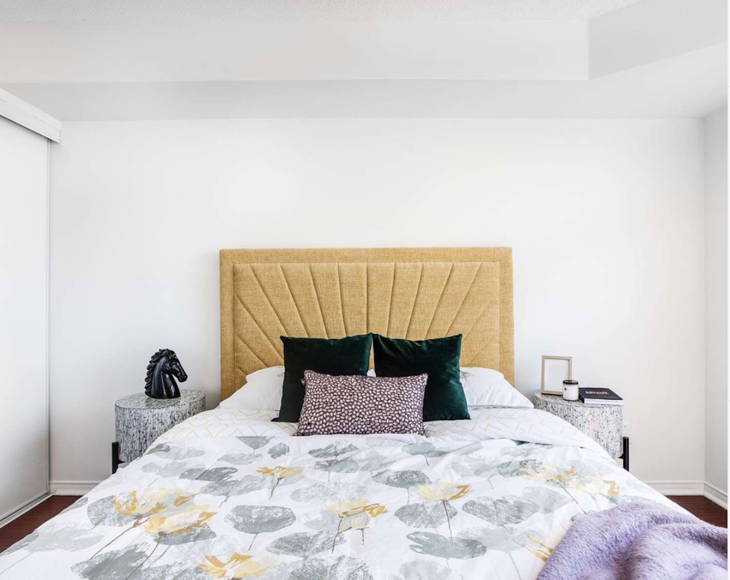 Schlafzimmer mit gelber und lila Farbgebung, grünen Akzentkissen und weißen Wänden,