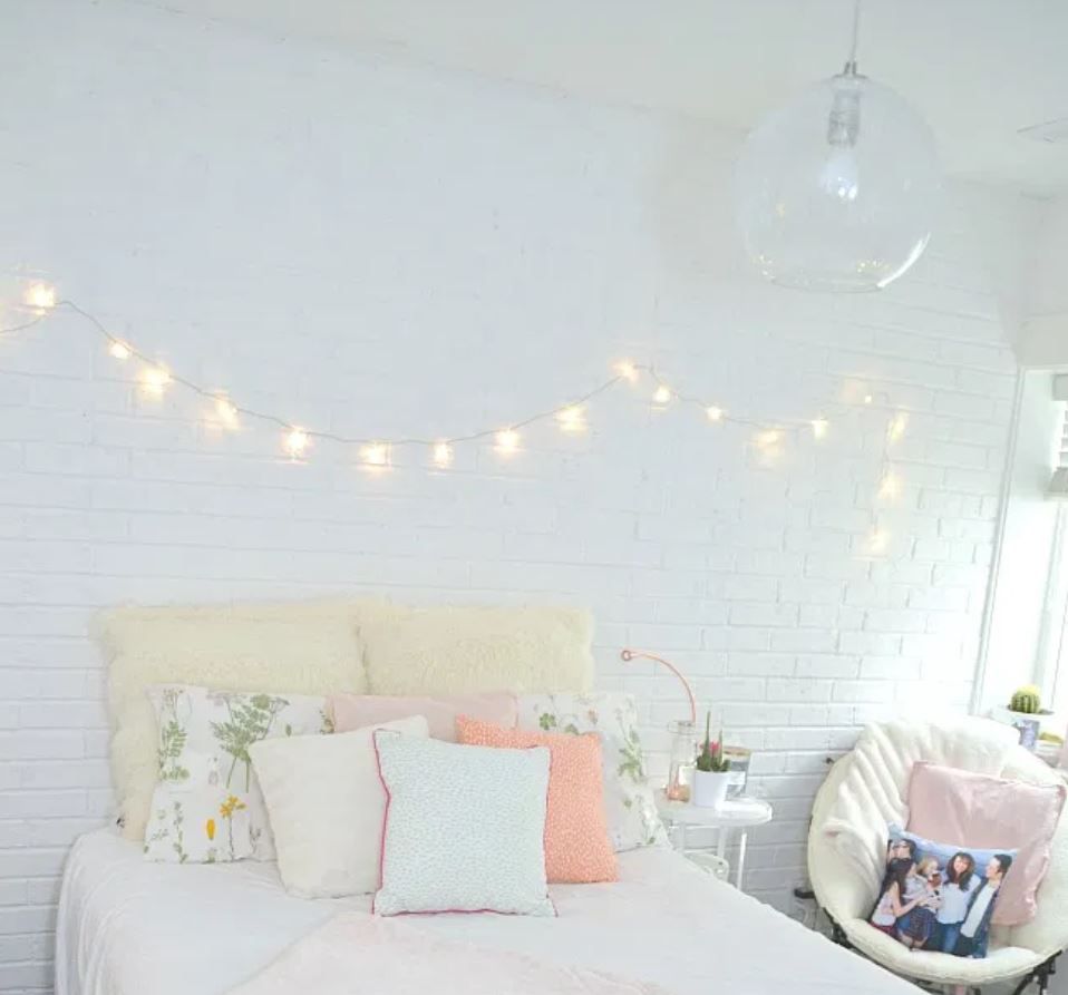 Teen girl's bedroom with white brick walls and stringlights over bed.