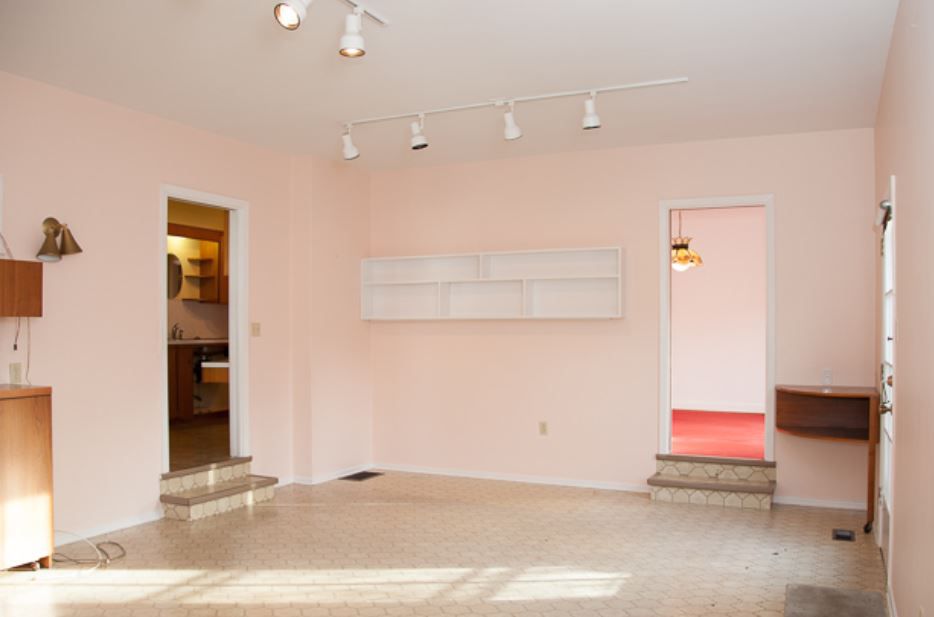Leeres Esszimmer mit hellen pfirsichfarbenen Wänden und weißer Schienenbeleuchtung.