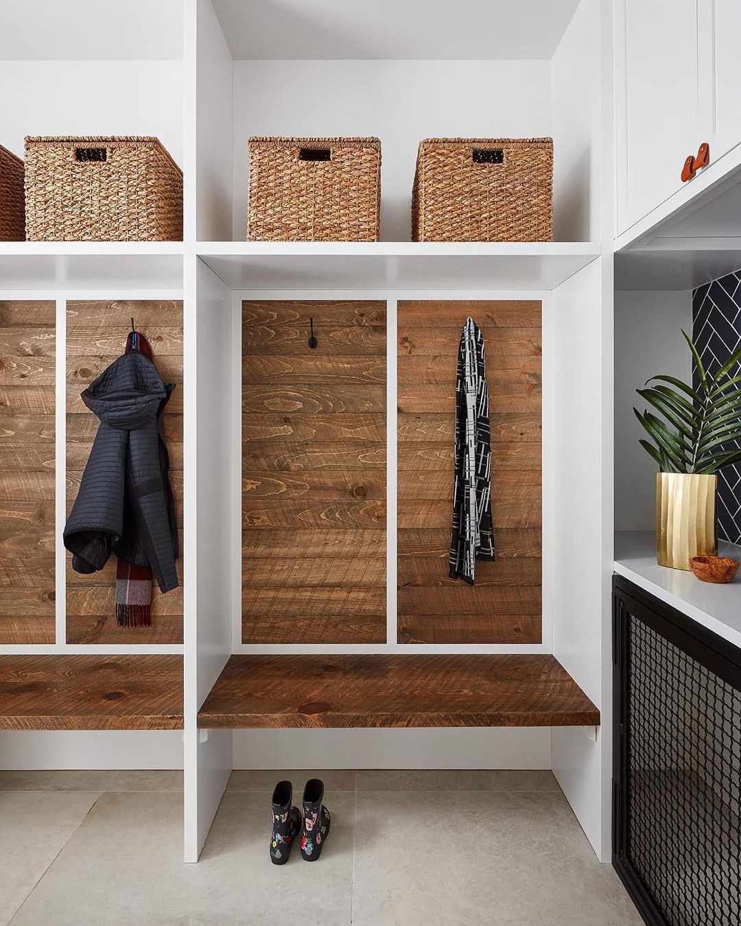 Un mudroom con zonas seccionadas acentuadas con madera envejecida, percheros y cubos de almacenaje abiertos en la parte superior.