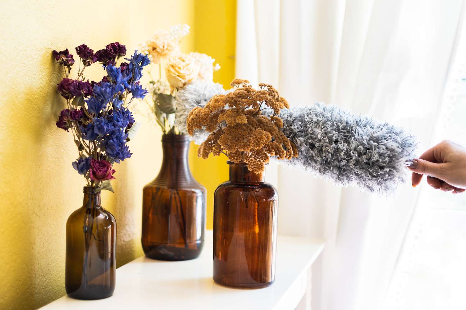 Getrocknete Blumensträuße in dunklen Glasvasen werden mit einem Staubtuch gereinigt