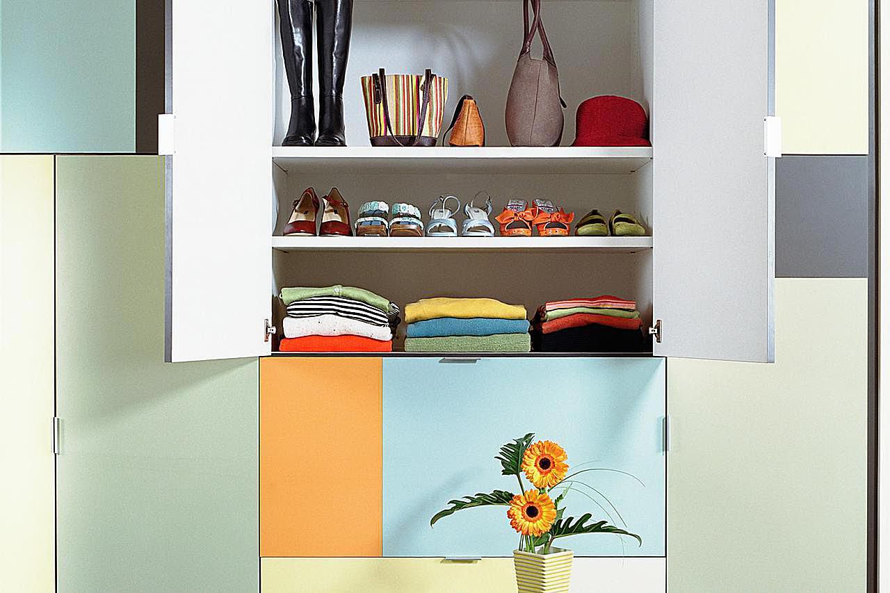 Open cupboard containing neatly stacked clothing in untidy room