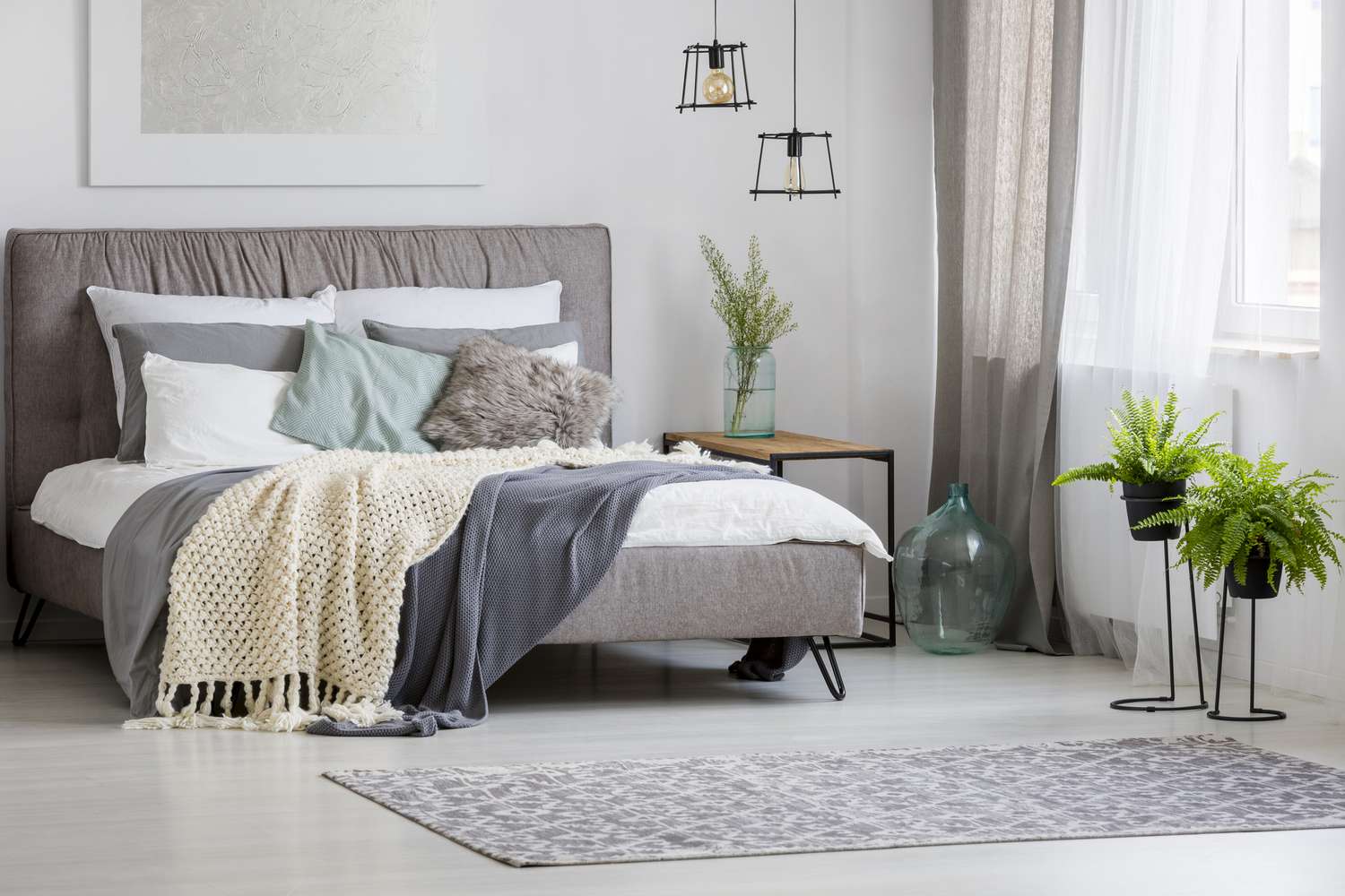 Graue, moderne Schlafzimmereinrichtung mit Kingsize-Bett, dekoriert mit Kissen und Decken