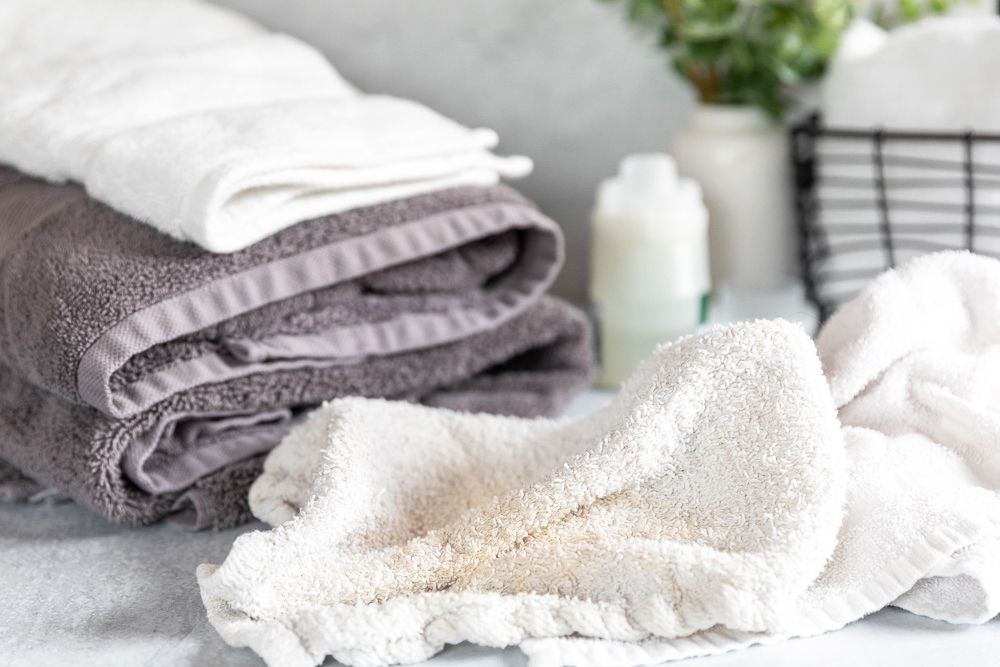 Zerknittertes weißes Handtuch mit braunem Fleck vor gefalteten sauberen Handtüchern 
