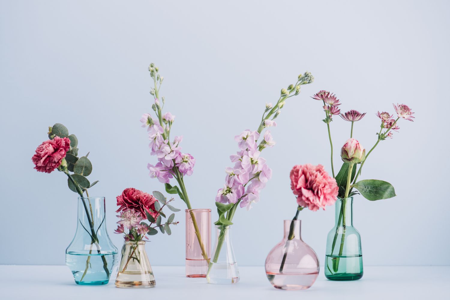 uma fileira de vasos de vidro de vários tamanhos e cores com flores