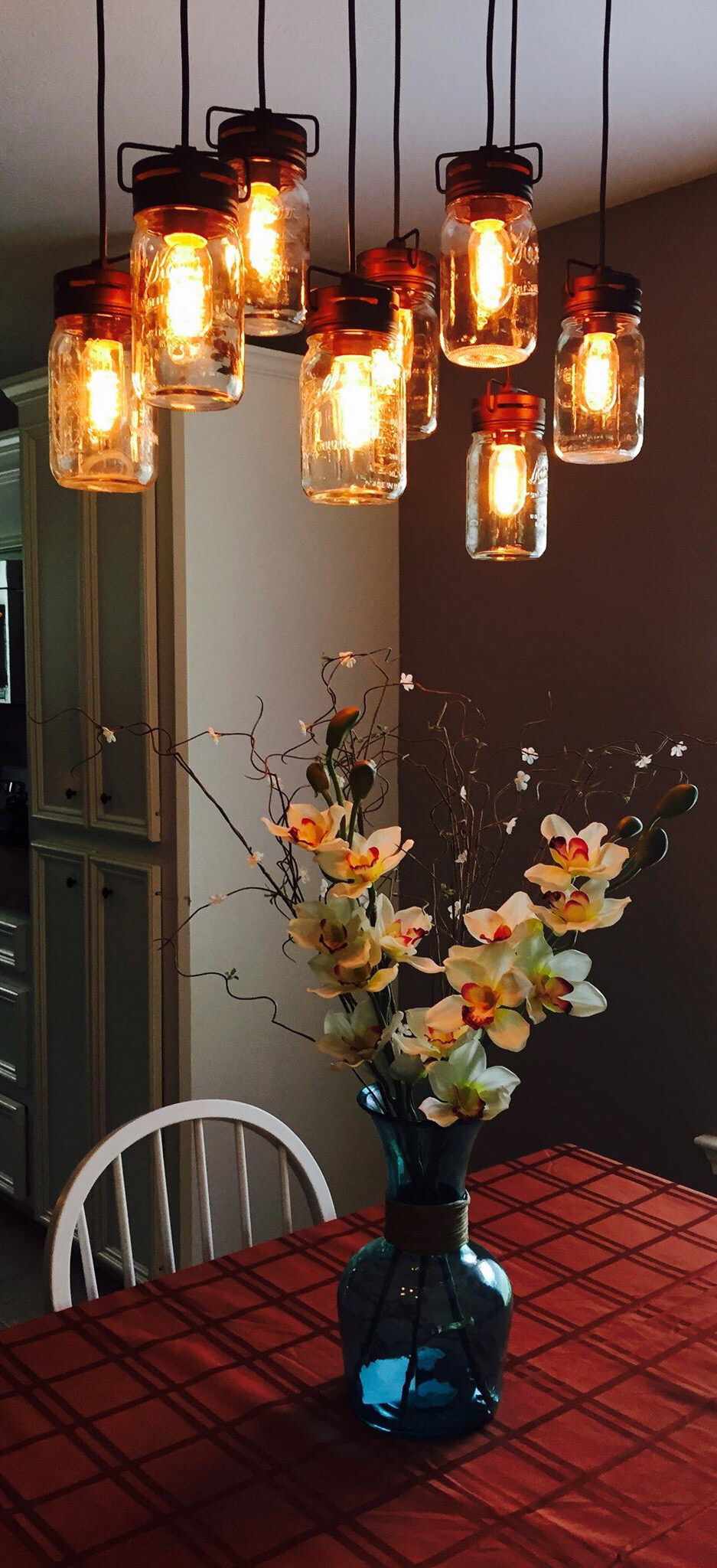 Table de cuisine confortable avec des lampes suspendues orange chaudes au-dessus d'une nappe rouge avec des fleurs dans un vase