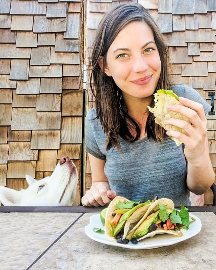 Person, die Gemüsetacos isst, während ein Hund daran schnüffelt