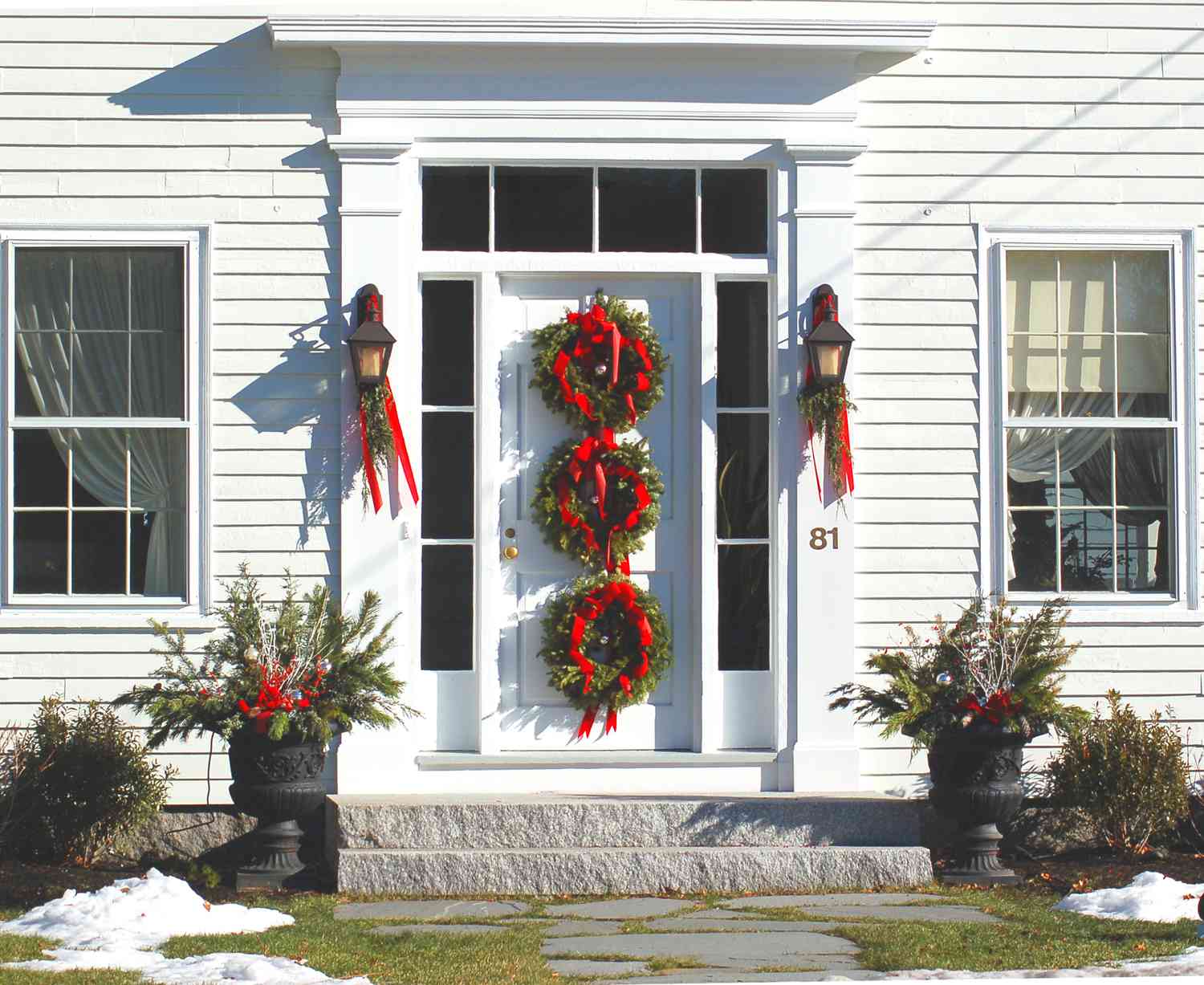 Image : 3 couronnes, guirlandes et urnes plantées décorent cette porte d'entrée à Noël.