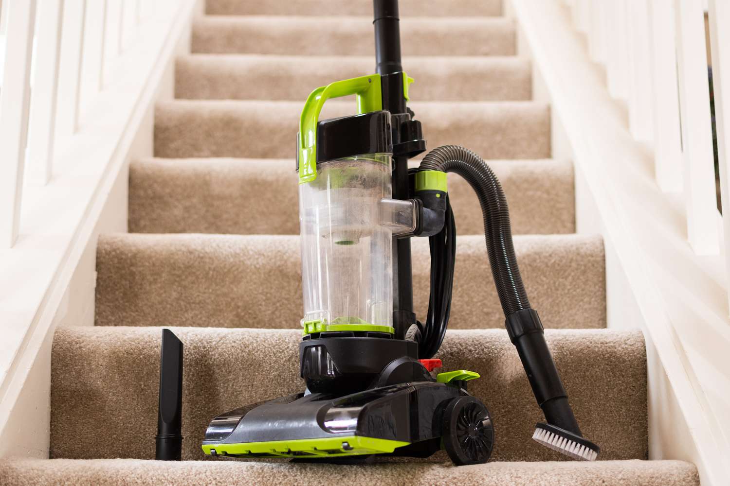 Cordless vacuum resting on bottom of carpetted stairs with attachments