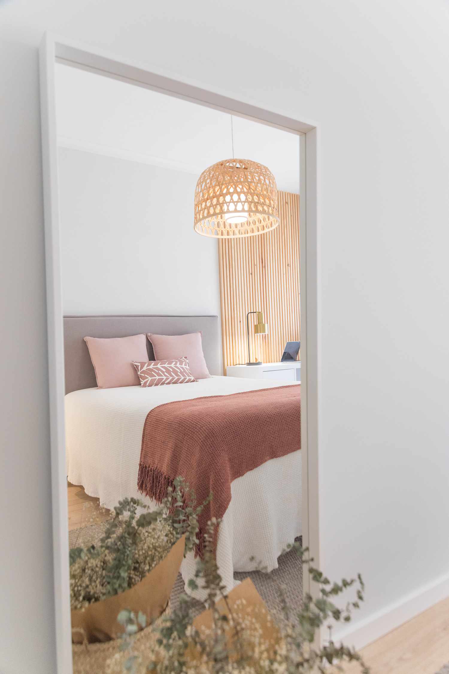 Espelho mostrando o reflexo de uma cama com travesseiros rosa e cobertor cor de ferrugem