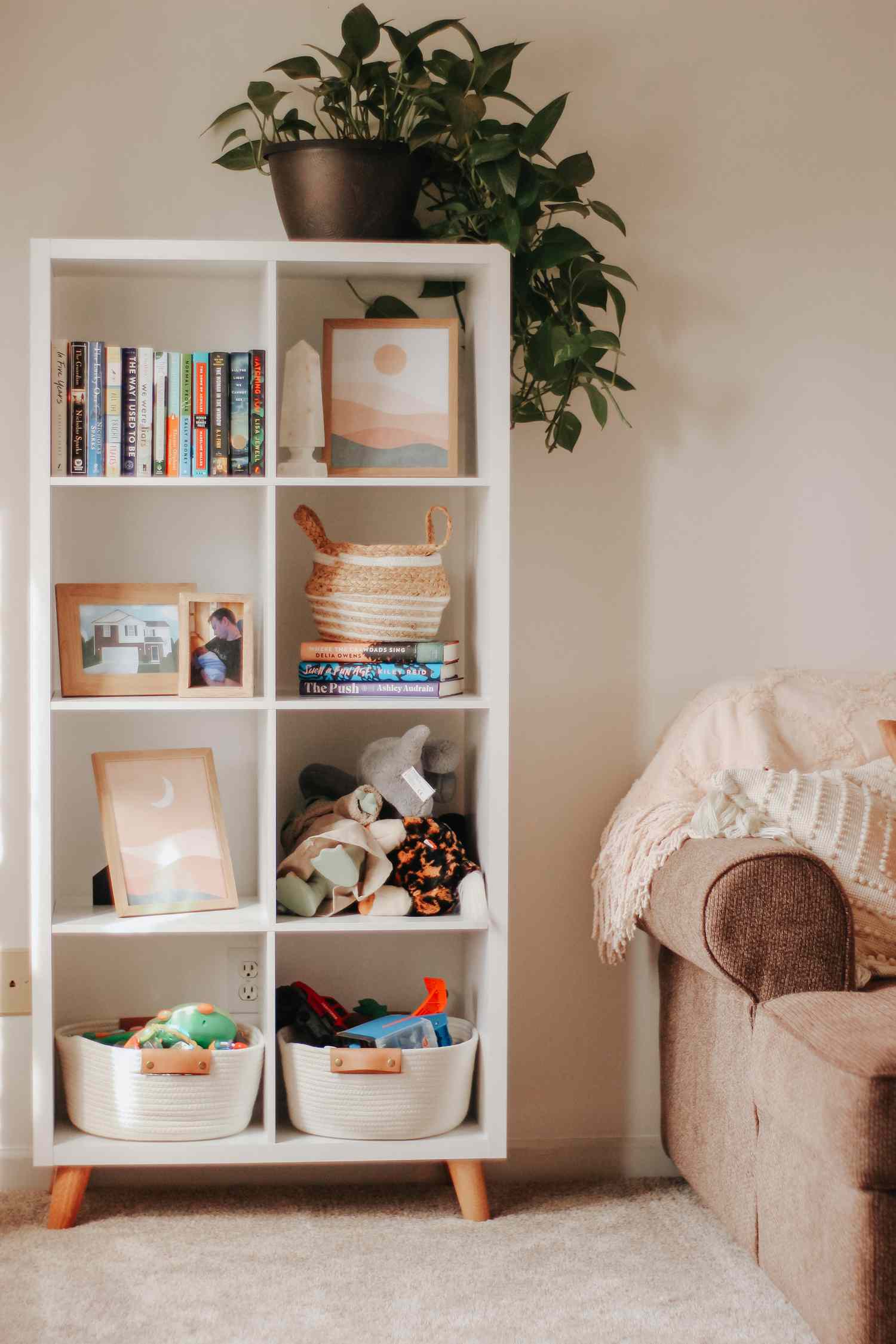 Weißes Bücherregal mit Holzbeinen, in dem Kunst und Spielzeug für Kleinkinder ausgestellt sind