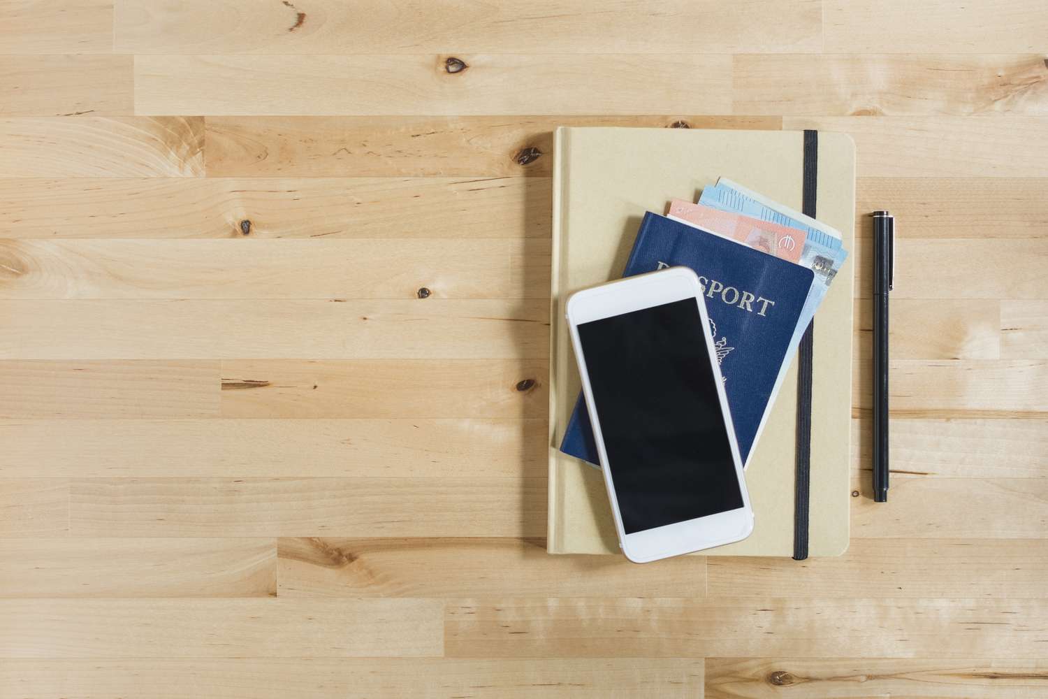 Tagebuch, Reisepass mit Papiergeld, Smartphone und Stift auf Holztisch