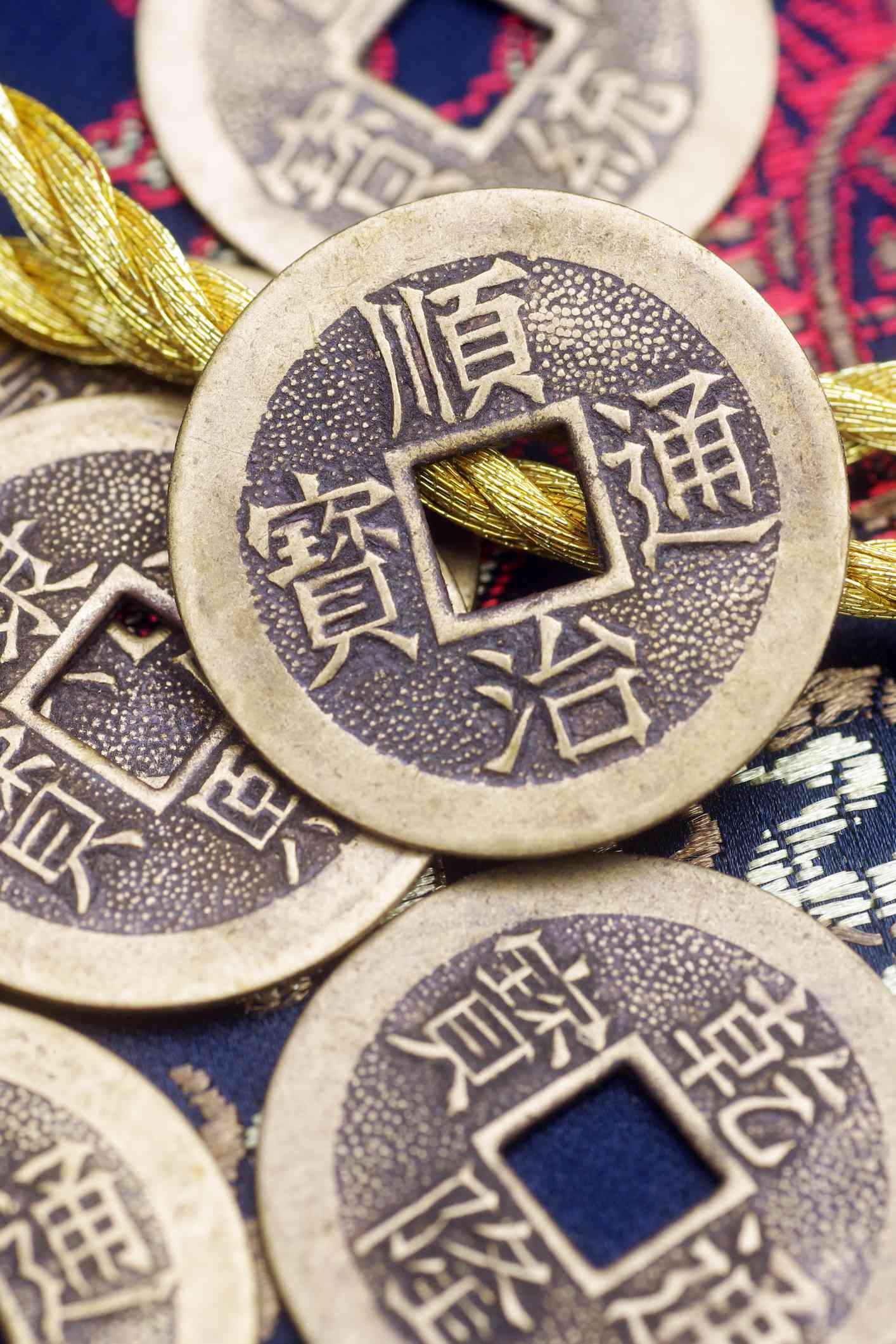 Antike chinesische Kupfermünzen auf einem gestickten Brokat-Hintergrund. Goldene gestickte Kordel im Hintergrund.