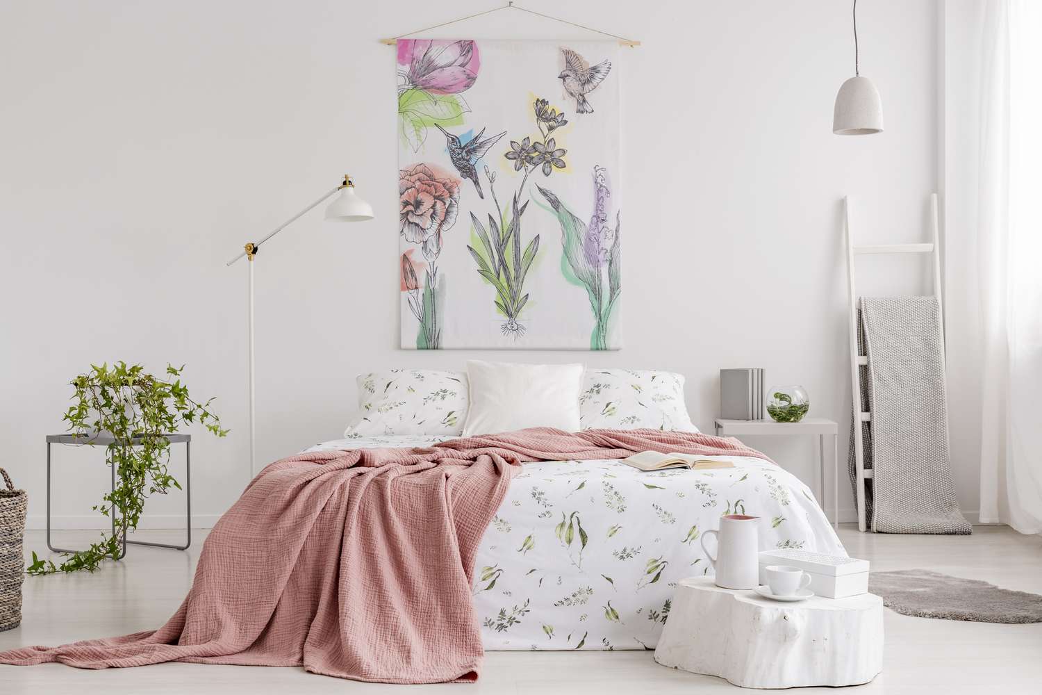 Couverture pêche et blanc avec motif vert lin sur le lit dans un intérieur de chambre naturelle et lumineuse. Tapisserie avec des fleurs colorées et des colibris sur le mur du fond.