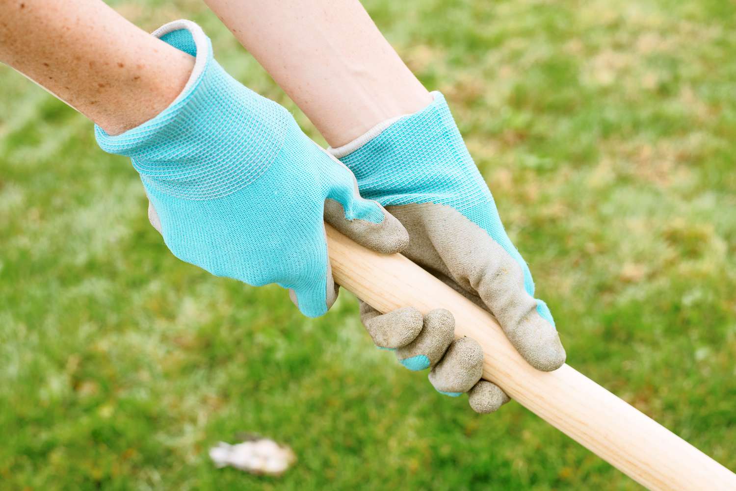 Blue and gray gloves being worn while holding on wooden handle