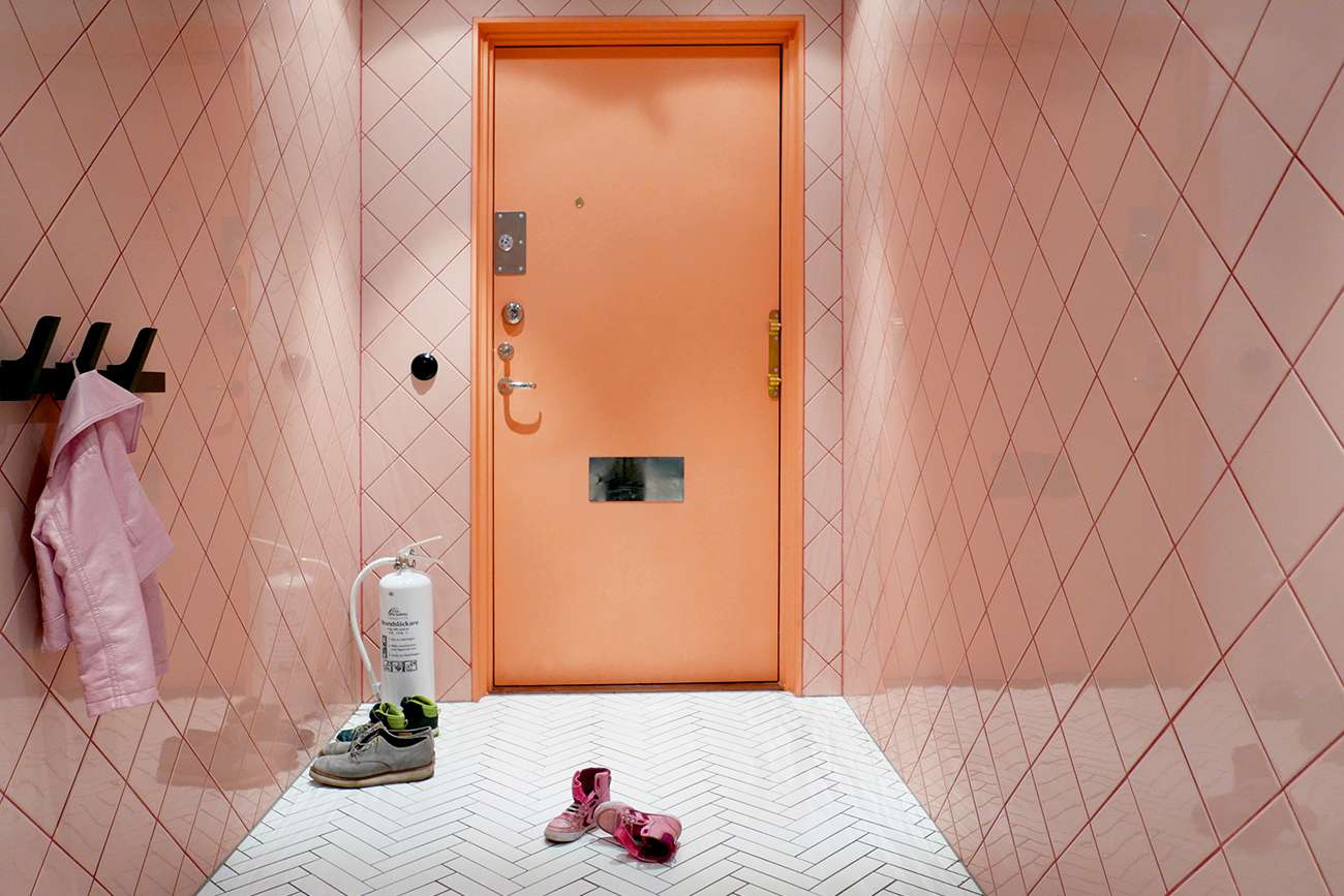 Entrada de apartamento com azulejos rosa e porta laranja