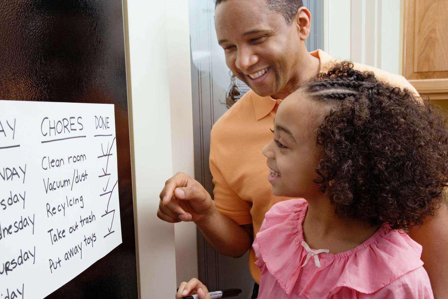 Um pai e uma filha sorrindo para uma tabela de tarefas