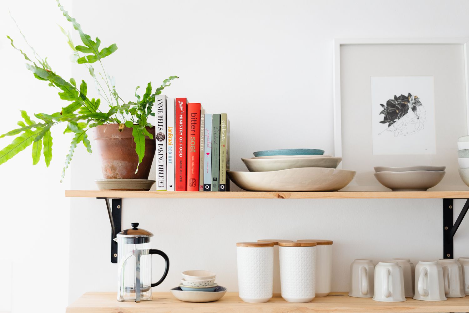 Prateleiras de madeira exibindo livros de receitas e plantas domésticas ao lado de utensílios de cozinha e cafeteira