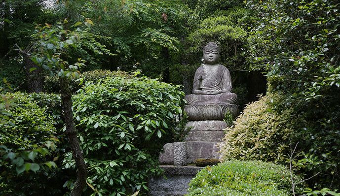 Buddha-Statue aus Stein, umgeben von grünen, belaubten Sträuchern und Bäumen in einem Park