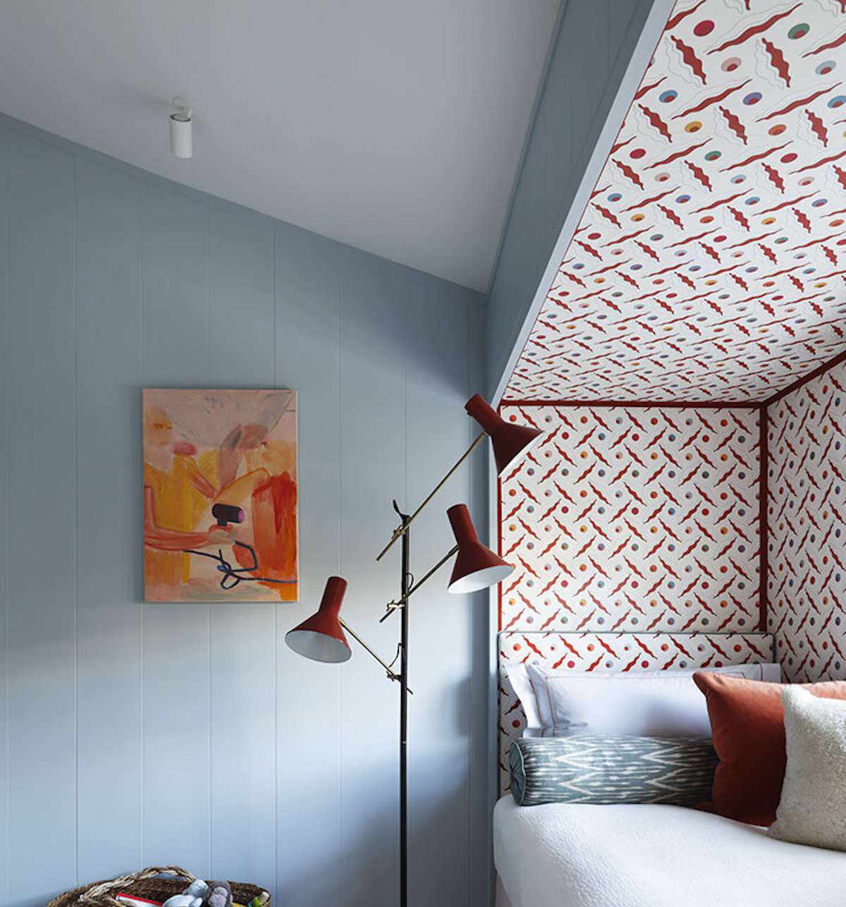 quarto com paredes azuis claras, padrão vermelho e branco em um canto com uma cama, luminária vermelha moderna